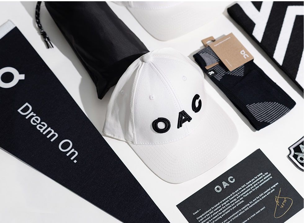 A flatlay of merch branded OAC, all in black and white and encompassing a pennant, ballcap, socks, and iron-on patch.